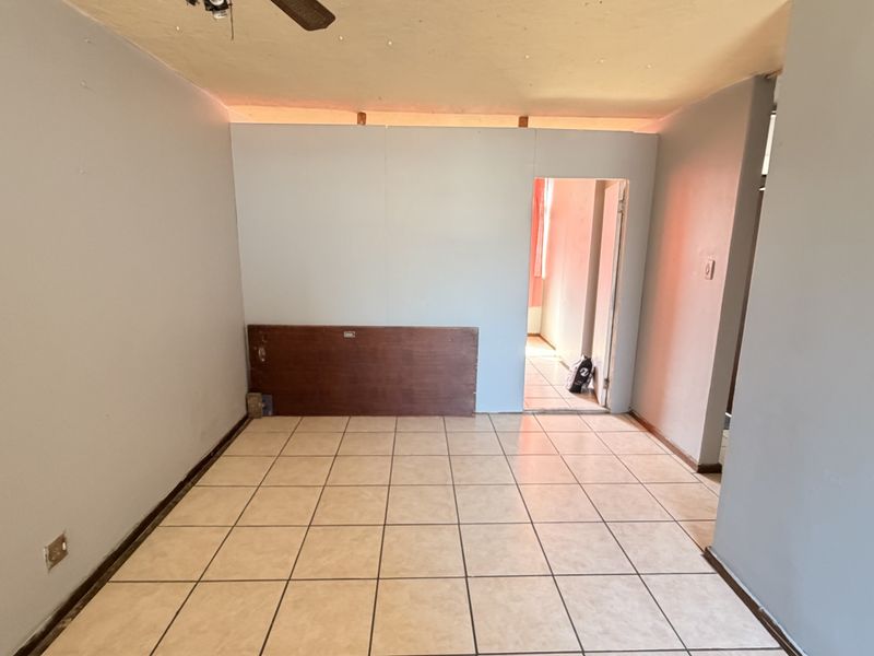 An empty living area featuring ceramic floor tiles, a ceiling fan, and an unfinished partition wall leading to an adjacent room.