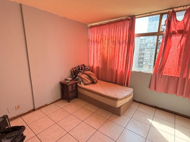 A bedroom featuring tiled flooring and a large window, providing natural light. The space requires cosmetic updates to improve its overall condition.