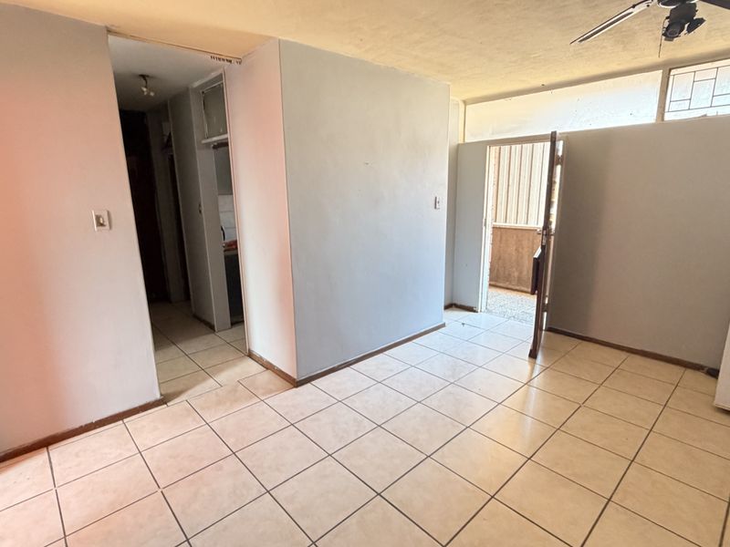 An empty living area featuring tiled flooring, a ceiling fan, and access to an outdoor space, offering a blank canvas for renovation.