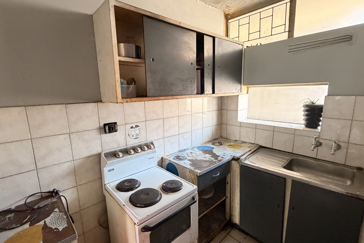 A compact kitchen featuring original cabinetry, a stainless steel sink, and a tiled splashback, currently requiring significant renovation and modernization.