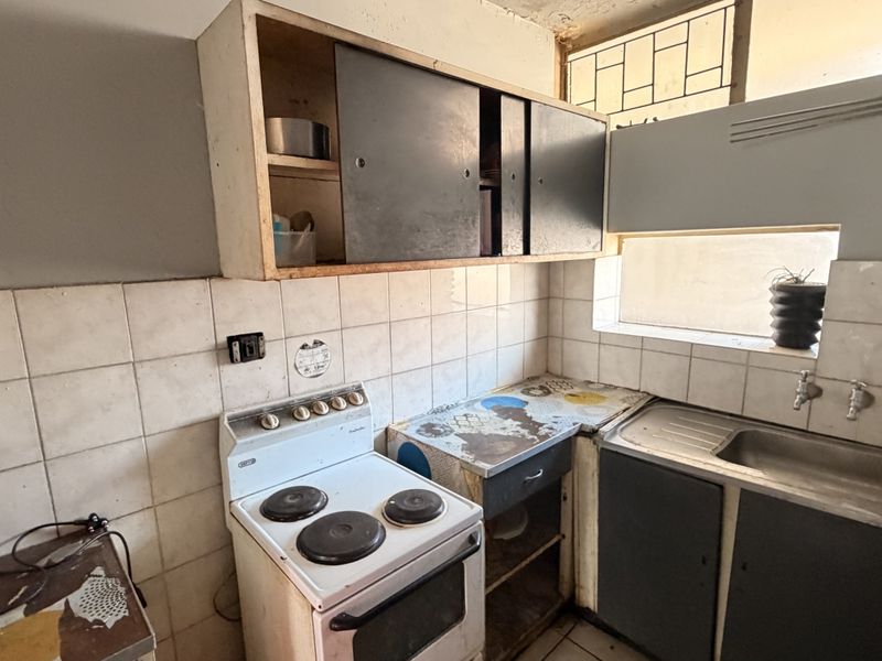 A compact kitchen featuring original cabinetry, a stainless steel sink, and a tiled splashback, currently requiring significant renovation and modernization.