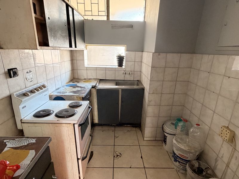 A dated kitchen featuring tiled walls and flooring, a stainless steel sink, and built-in cabinetry, requiring significant renovation to modernize the space.