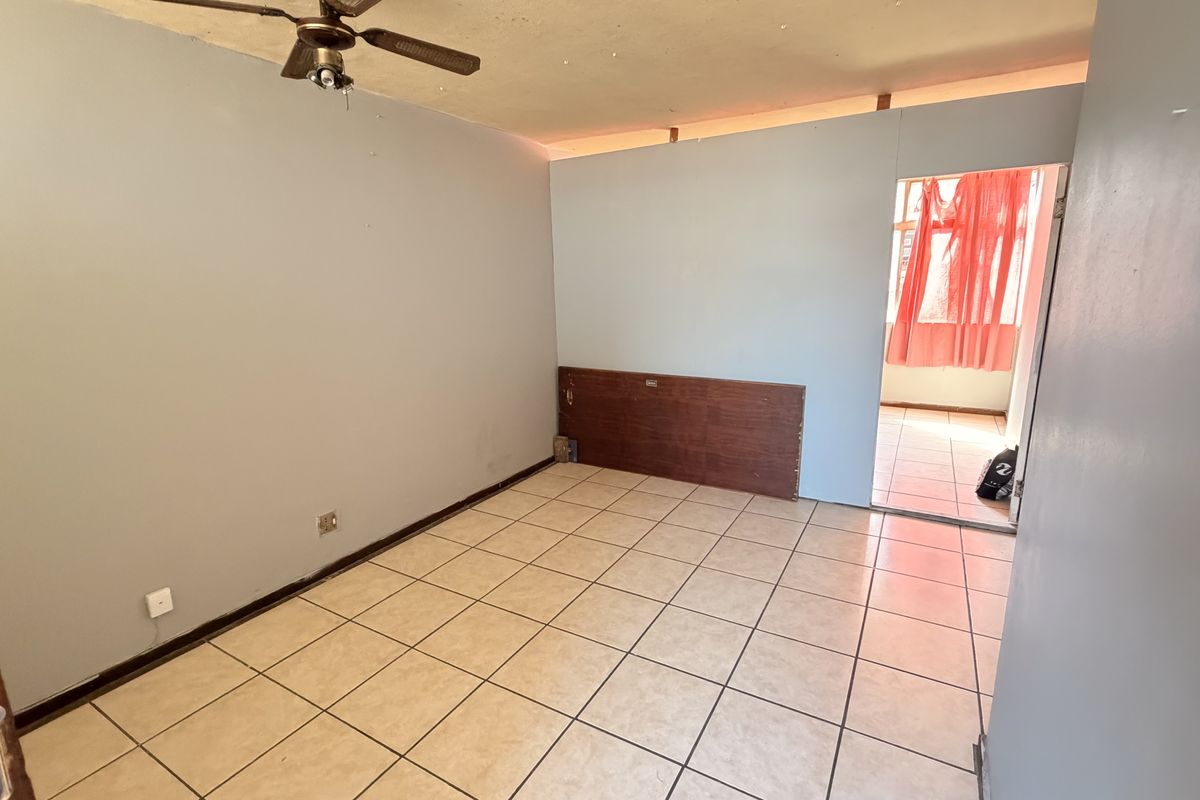An empty bedroom featuring tiled flooring, a ceiling fan, and a built-in headboard, requiring minor cosmetic updates to the walls and ceiling.