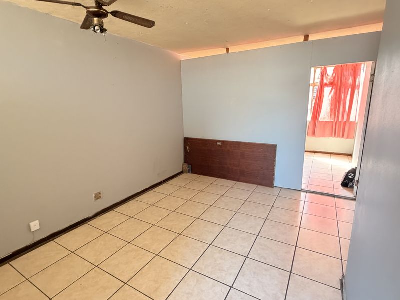 An empty bedroom featuring tiled flooring, a ceiling fan, and a built-in headboard, requiring minor cosmetic updates to the walls and ceiling.