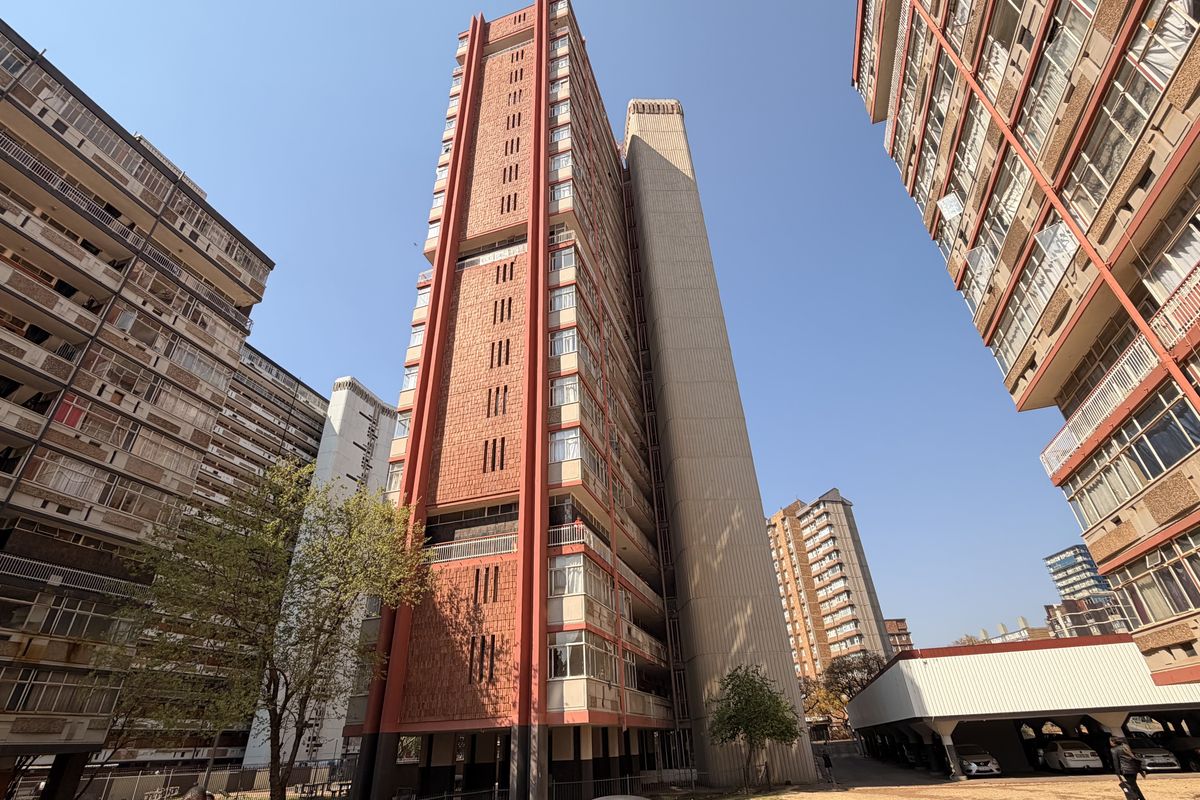 Exterior view of a high-rise residential apartment complex featuring a multi-story facade with balconies and an adjacent covered parking structure.