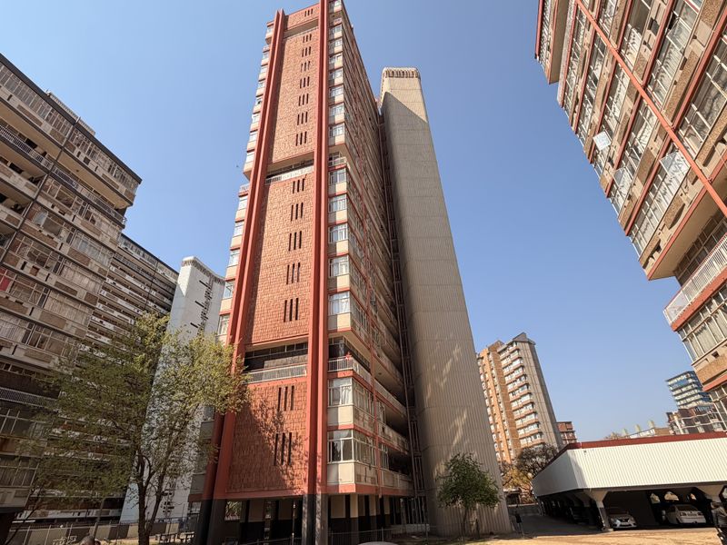 Exterior view of a high-rise residential apartment complex featuring a multi-story facade with balconies and an adjacent covered parking structure.