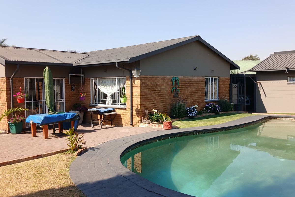 Rear exterior view of the house featuring a brick facade, metal roof, and a curved swimming pool with surrounding brick paving.