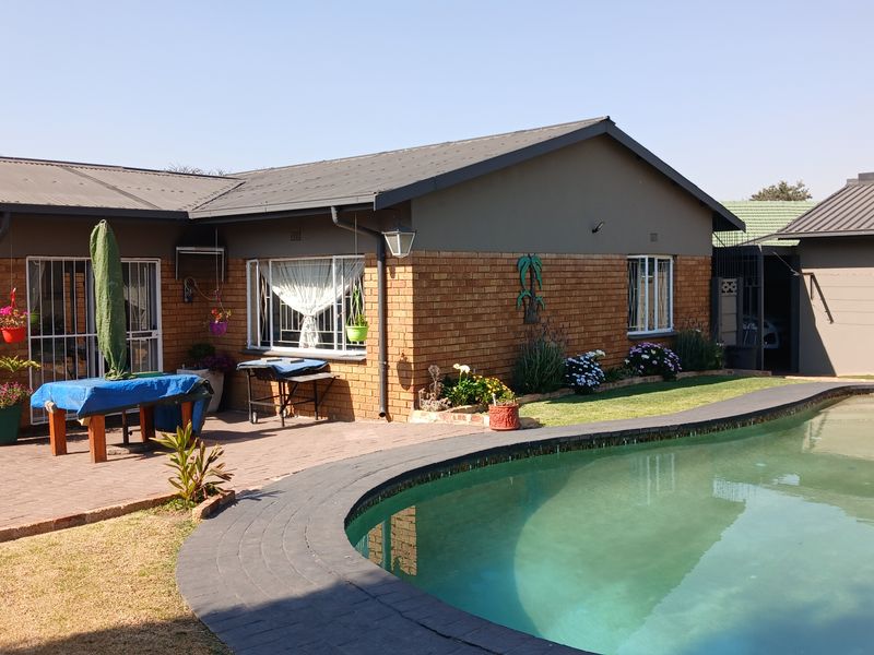 Rear exterior view of the house featuring a brick facade, metal roof, and a curved swimming pool with surrounding brick paving.