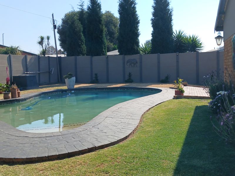 A private backyard featuring a swimming pool with a paved surround, established lawn, and secure precast concrete boundary walling.