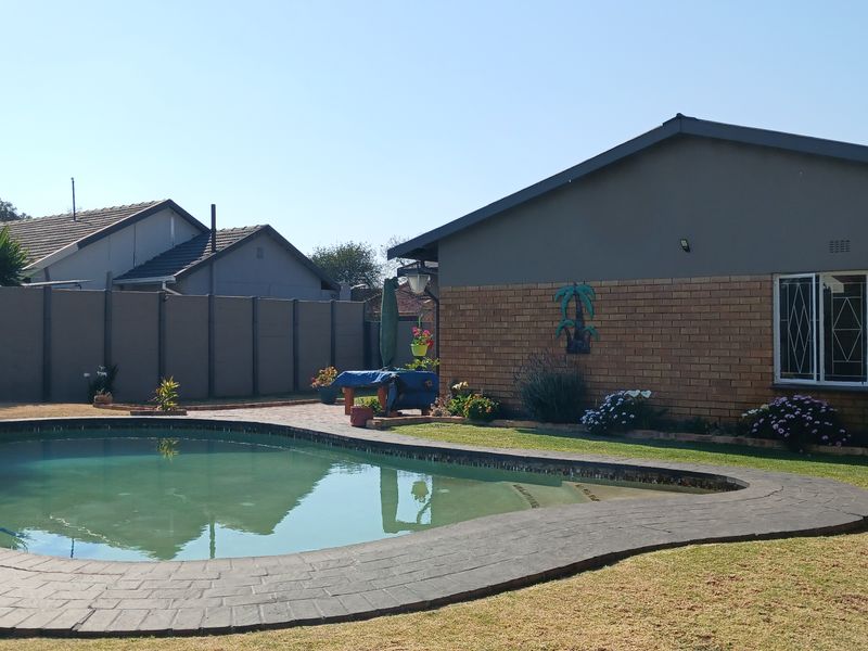 A backyard area featuring a swimming pool with a paved surround, set against a brick and rendered exterior wall with security-fitted windows.