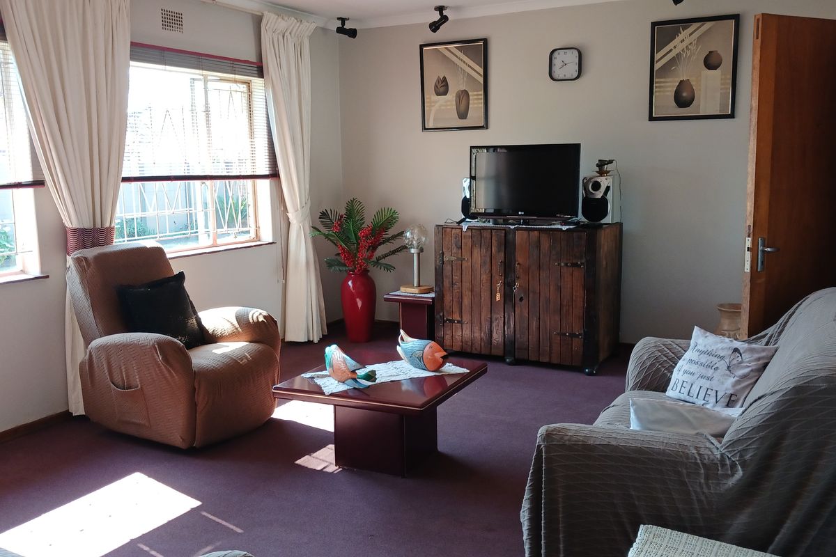 A comfortable living room featuring carpeted flooring, coving, and large windows fitted with security burglar bars.