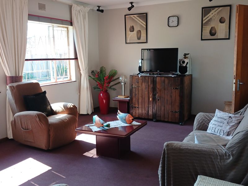 A comfortable living room featuring carpeted flooring, coving, and large windows fitted with security burglar bars.