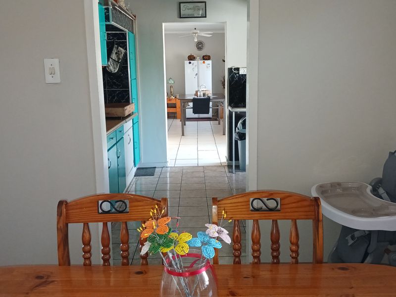 A view through to a functional kitchen featuring tiled flooring and fitted cabinetry, connecting to an adjacent dining area.