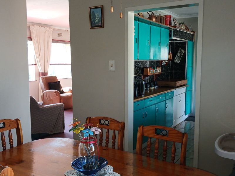 Open plan dining area leading into a functional kitchen with turquoise cabinetry and dark tiled backsplash.