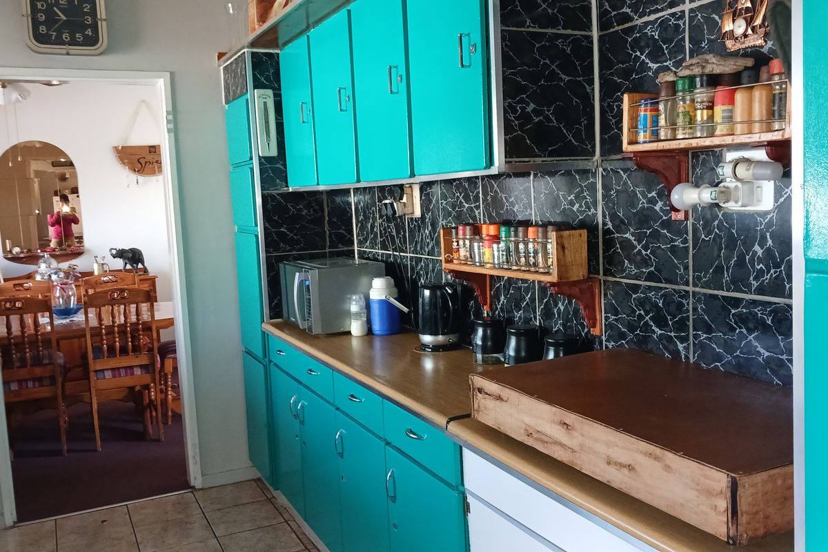 A dated kitchen featuring bright teal cabinetry, dark marble-effect tiled backsplash, and laminate countertops, with an adjacent view into the dining area.