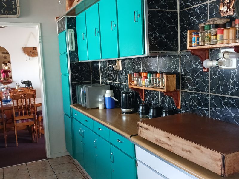 A dated kitchen featuring bright teal cabinetry, dark marble-effect tiled backsplash, and laminate countertops, with an adjacent view into the dining area.
