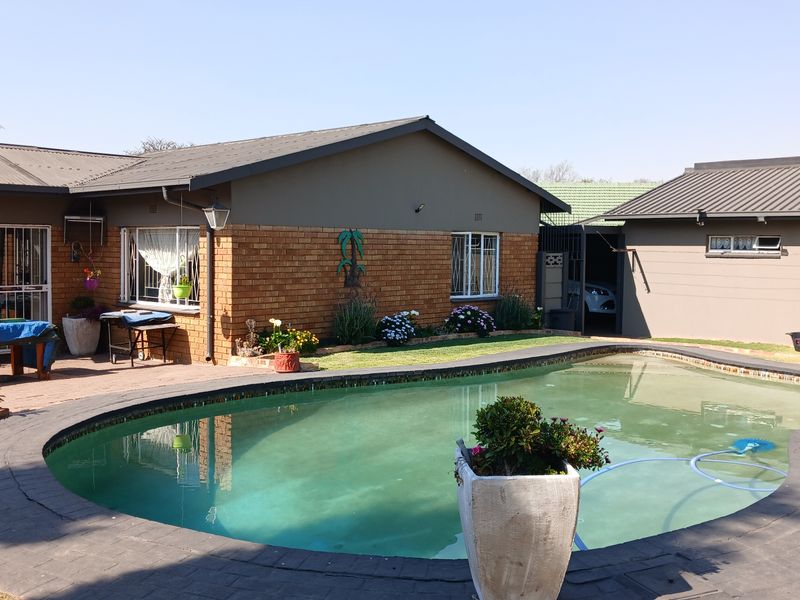 Rear exterior view featuring a swimming pool with brick paving and a brick-faced house structure with a metal roof.