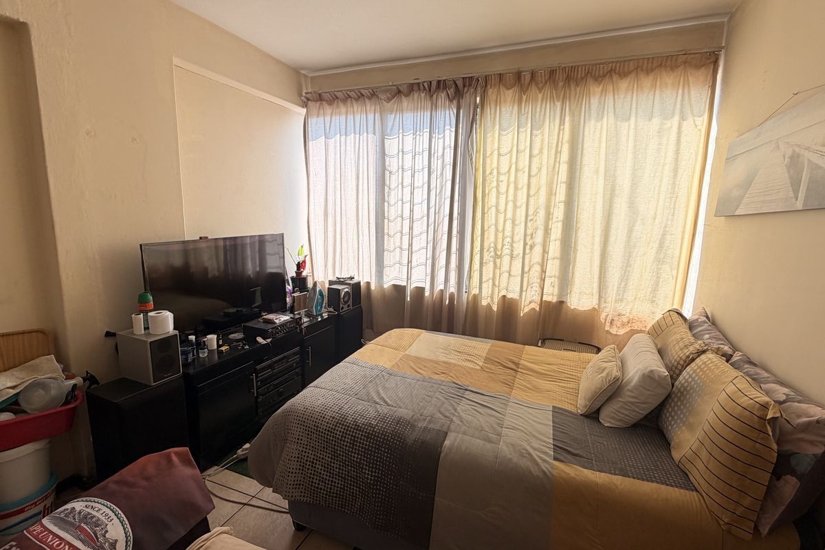 A bedroom featuring tiled flooring and a large window, currently showing signs of wear on the walls and plaster.