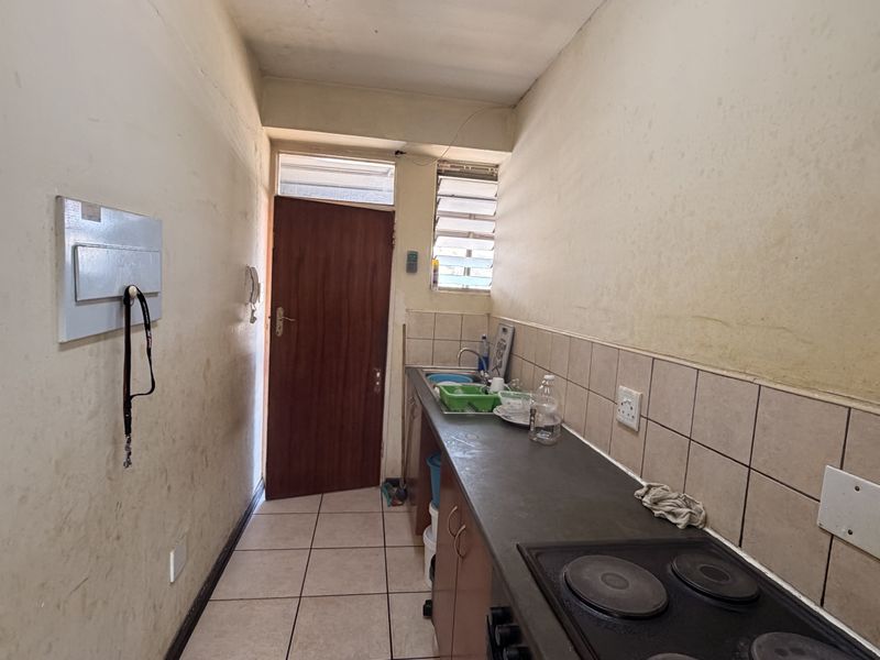 A compact kitchen featuring built-in cabinetry, a tiled backsplash, and an electric hob, requiring cosmetic updates to improve its overall condition.