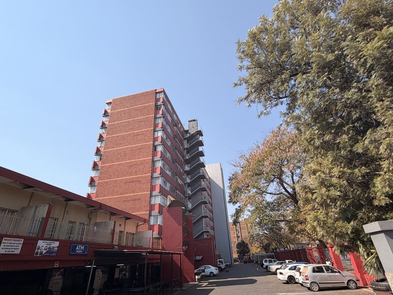 Exterior view of a multi-story residential apartment building featuring a prominent external fire escape staircase and paved driveway access.