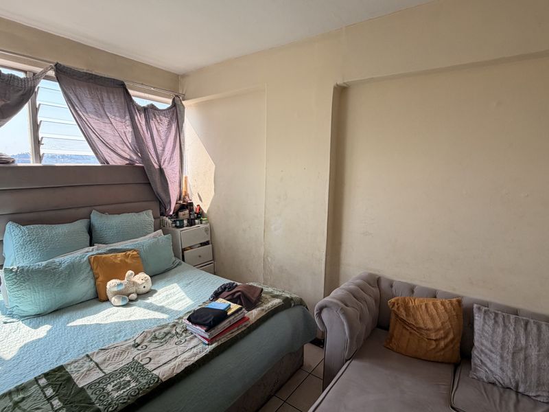 A bedroom featuring tiled flooring and louvered windows with natural light, requiring cosmetic updates to the wall finishes.