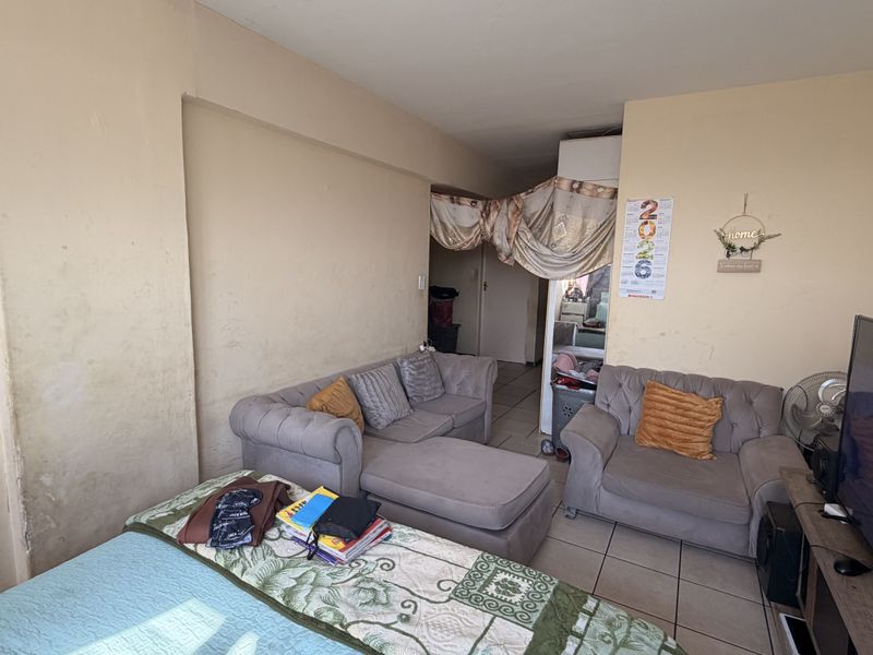 A living room area featuring tiled flooring and walls showing signs of wear and staining, requiring cosmetic attention.