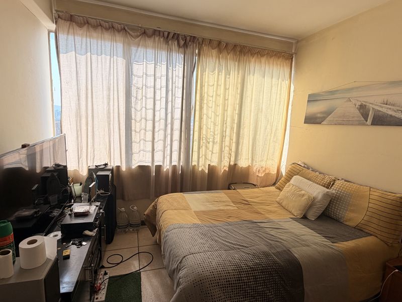 A bedroom featuring tiled flooring and a large window with curtains, providing natural light to the space.
