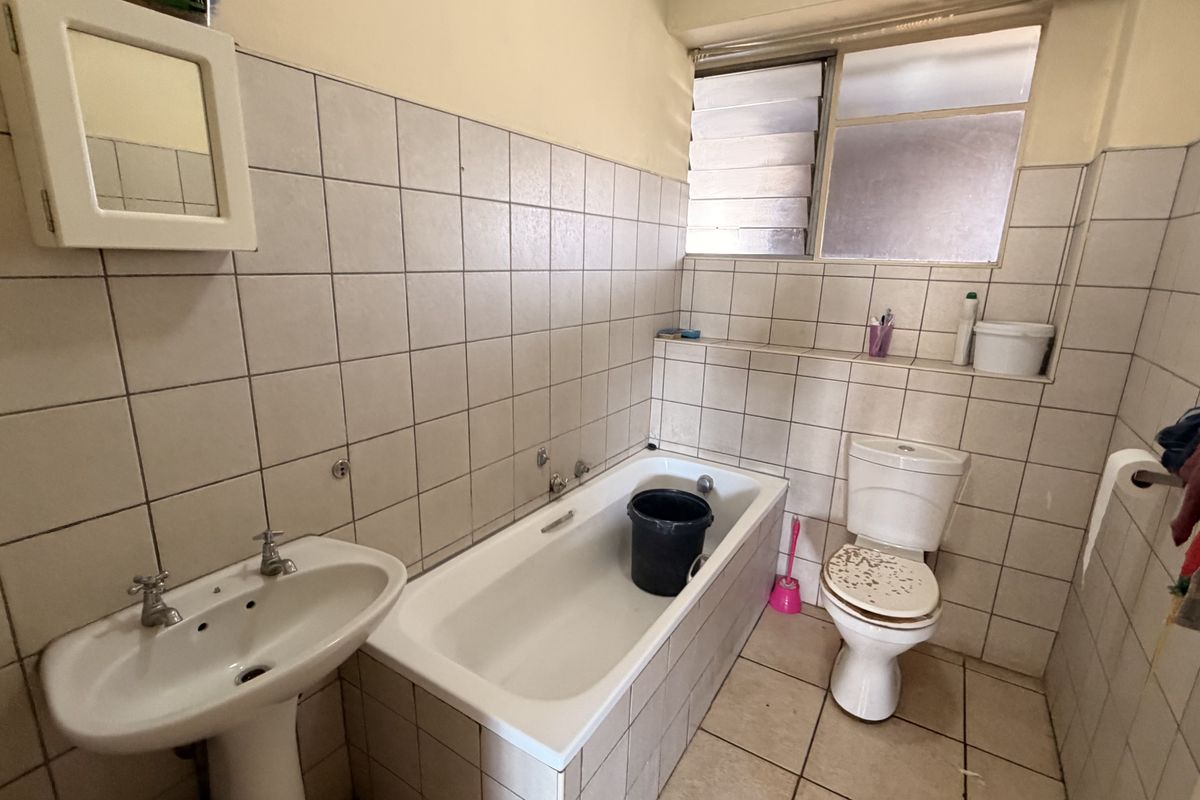 A dated bathroom featuring a pedestal basin, bathtub, and toilet with original ceramic wall tiling and louvered windows.