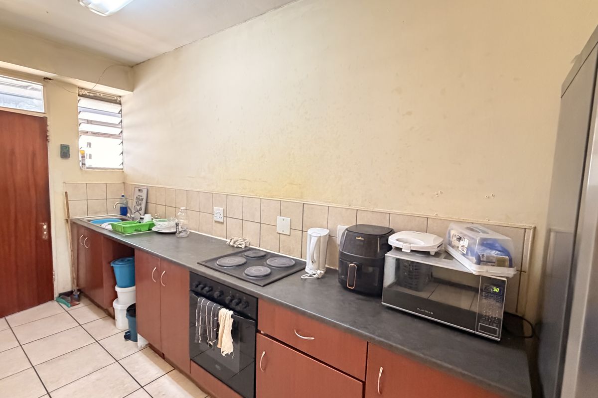 A functional kitchen featuring built-in cabinetry, an electric hob, oven, and tiled backsplash, requiring cosmetic updates to improve its overall condition.
