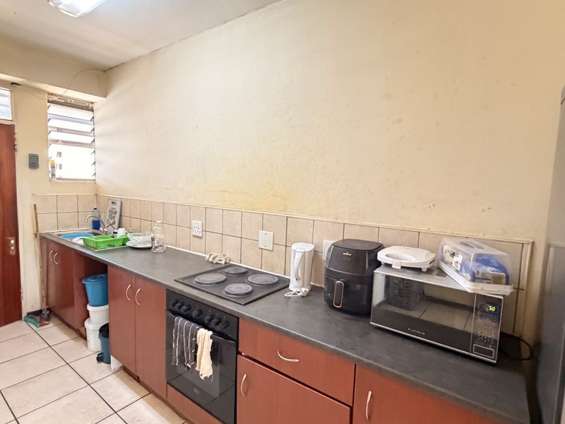 A functional kitchen featuring built-in cabinetry, an electric hob, oven, and tiled backsplash, requiring cosmetic updates to improve its overall condition.