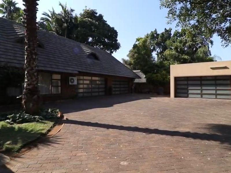 Spacious front exterior featuring a large paved driveway, a main house with a thatched roof, and a separate modern garage structure.