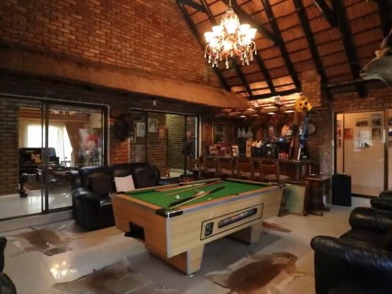 Spacious entertainment area featuring a built-in bar, exposed brick walls, and a high thatched ceiling with exposed timber trusses.