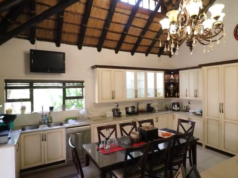 Spacious open-plan kitchen and dining area featuring a high thatched ceiling with exposed timber beams and traditional cabinetry.