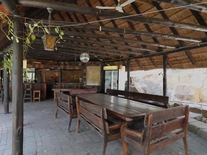 Spacious outdoor entertainment area featuring a traditional thatched roof, exposed timber beams, built-in bar, and brick paving, ideal for hosting gatherings.