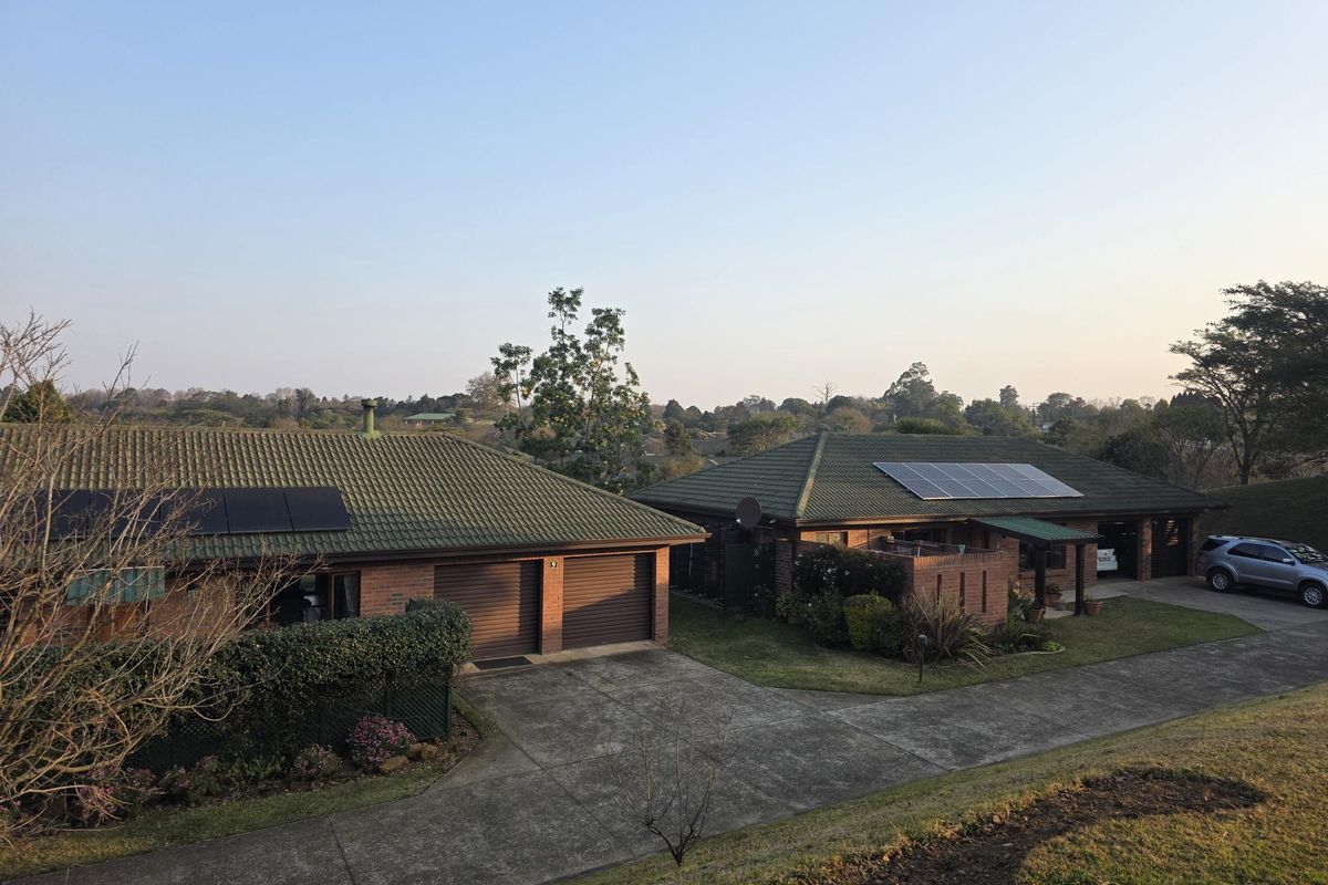 An elevated view of a brick townhouse complex featuring tiled roofs, solar panel installations, and paved driveways set within a landscaped estate.