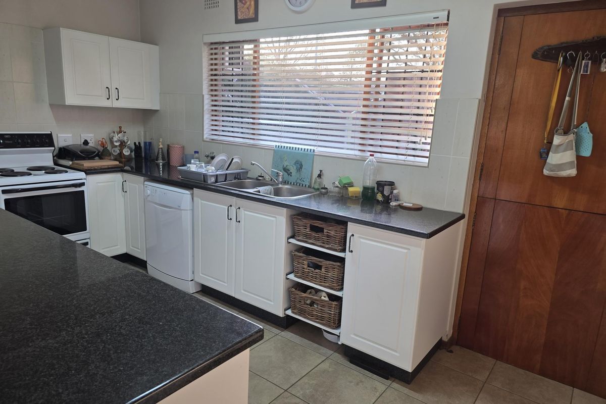 A functional kitchen featuring white cabinetry, dark granite countertops, a stainless steel double sink, and tiled flooring with a tiled splashback.