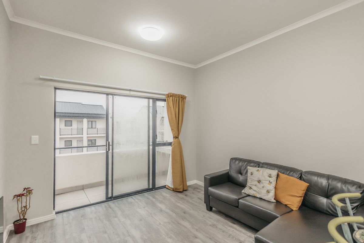 A bright living room featuring modern laminate flooring and a large sliding glass door providing access to an outdoor balcony area.