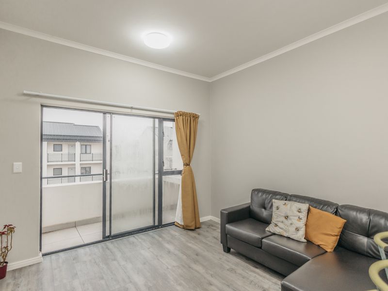 A bright living room featuring modern laminate flooring and a large sliding glass door providing access to an outdoor balcony area.