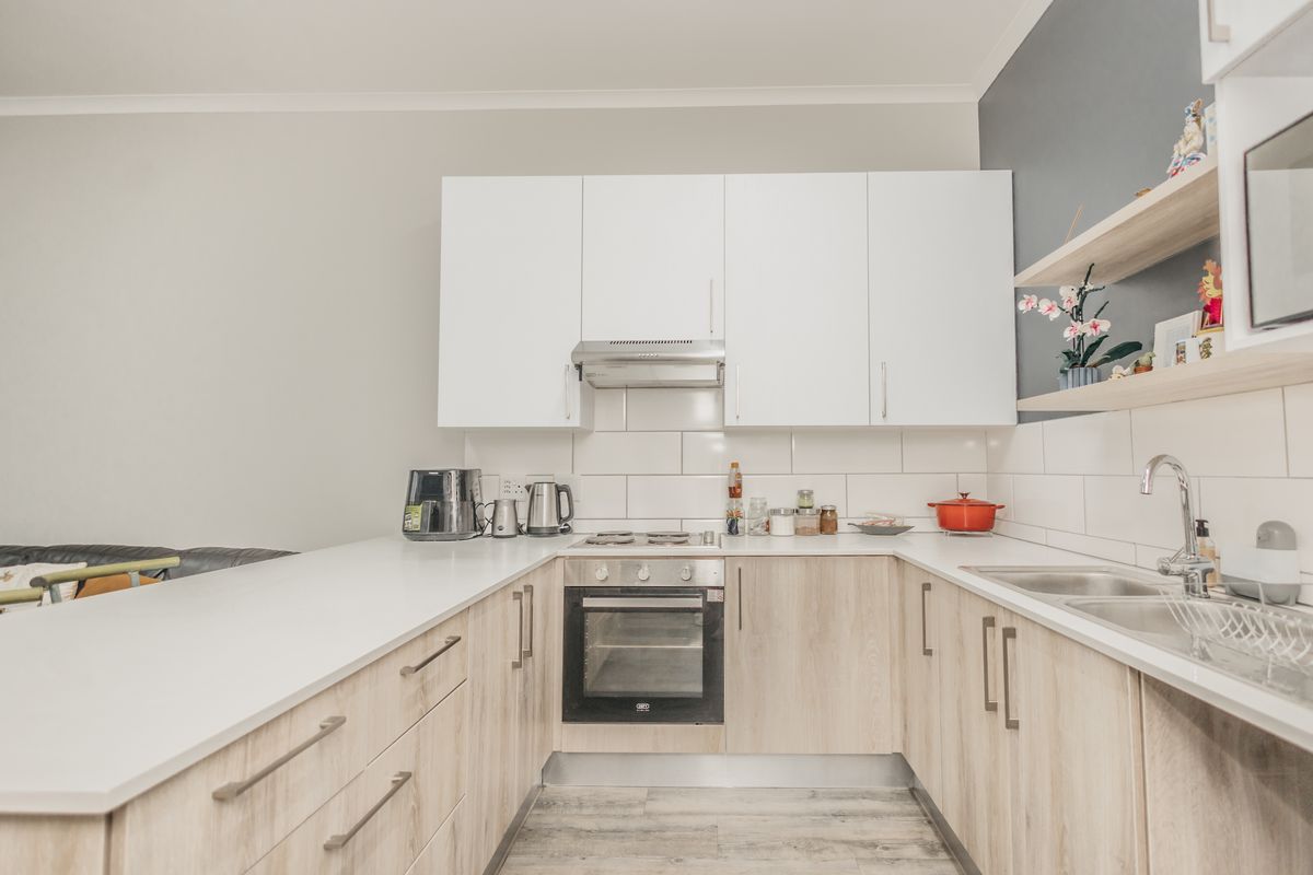 A modern, well-maintained kitchen featuring white and wood-look cabinetry, subway tile backsplash, built-in oven, and a clean quartz countertop.