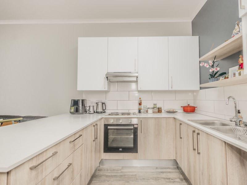 A modern, well-maintained kitchen featuring white and wood-look cabinetry, subway tile backsplash, built-in oven, and a clean quartz countertop.