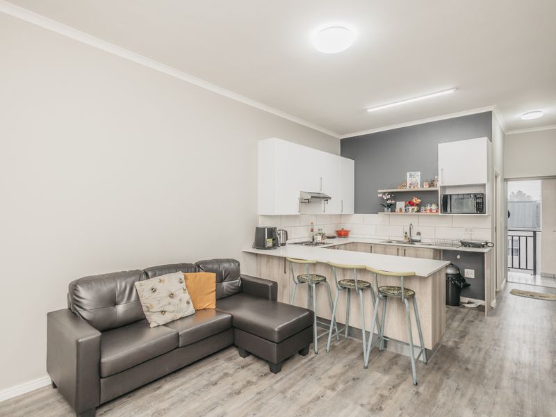 Open-plan living area featuring a modern kitchen with white cabinetry, a breakfast bar, and durable laminate flooring, leading to an outdoor balcony.