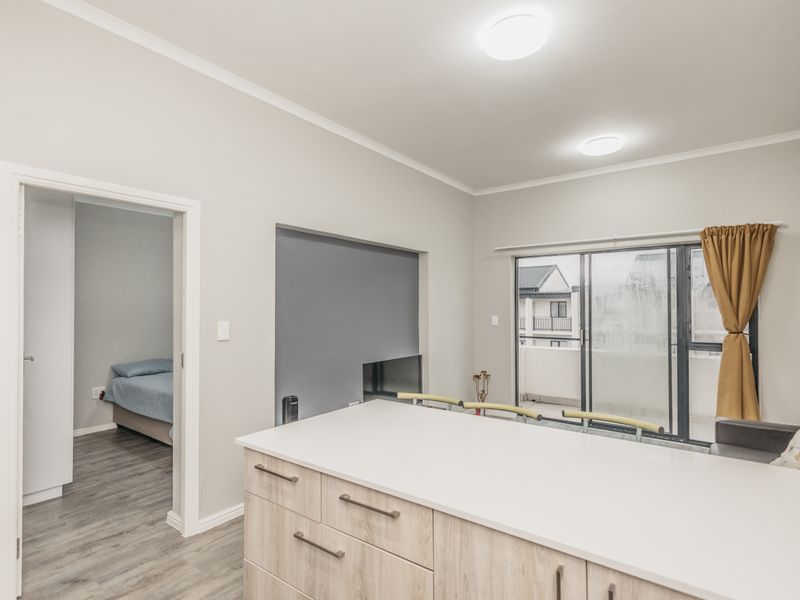 Open plan living area featuring a modern kitchen island, laminate flooring, and sliding glass doors leading to a balcony, with an adjacent bedroom visible.