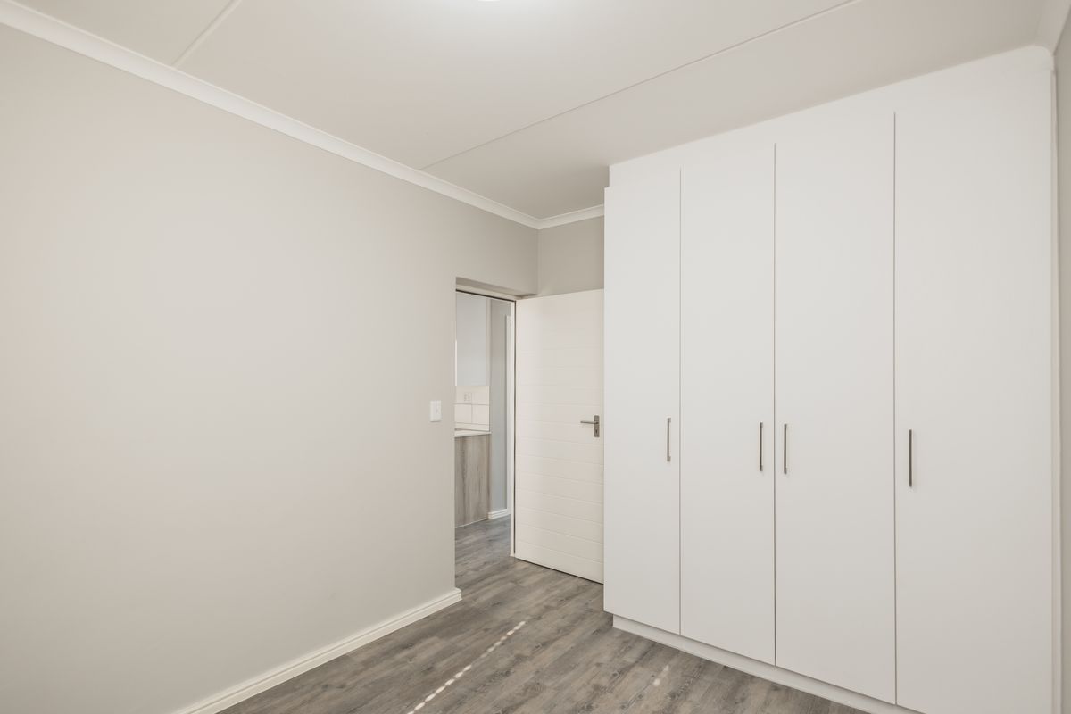 A clean, modern bedroom featuring neutral walls, durable laminate flooring, and ample built-in cupboard storage space.