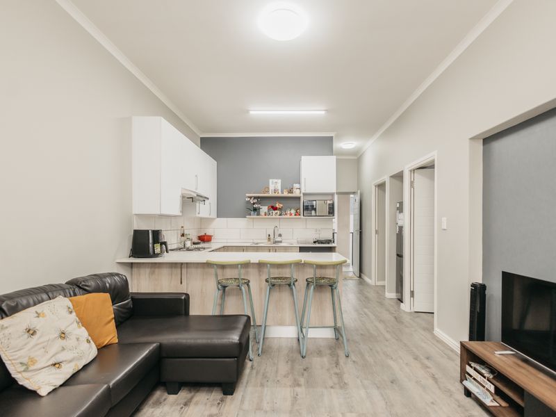 Open-plan living area featuring a modern kitchen with white cabinetry, light wood-look laminate flooring, and a functional breakfast bar layout.