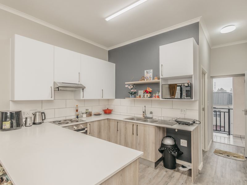 Modern kitchen featuring white and wood-tone cabinetry, subway tile backsplash, integrated appliances, and a breakfast bar, leading to an outdoor balcony area.
