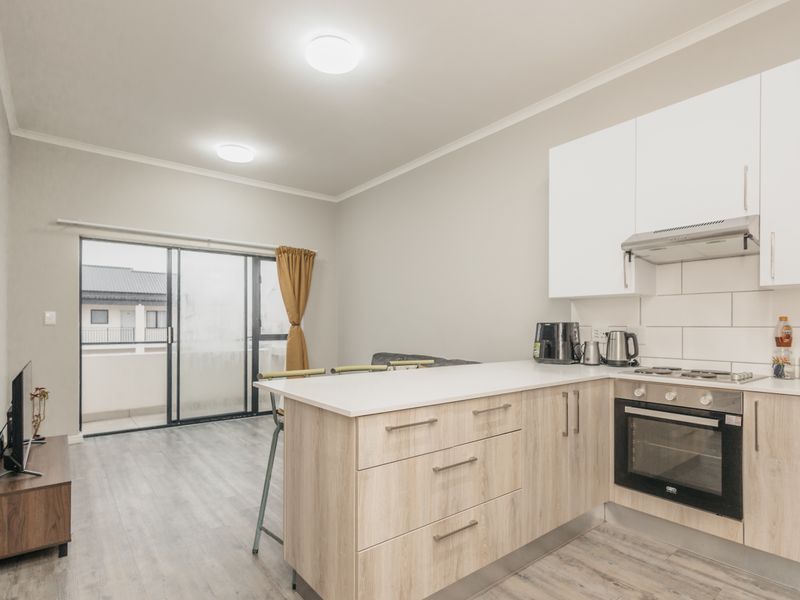 Modern open-plan kitchen and living area featuring light wood cabinetry, integrated appliances, subway tile backsplash, and direct access to a private balcony.