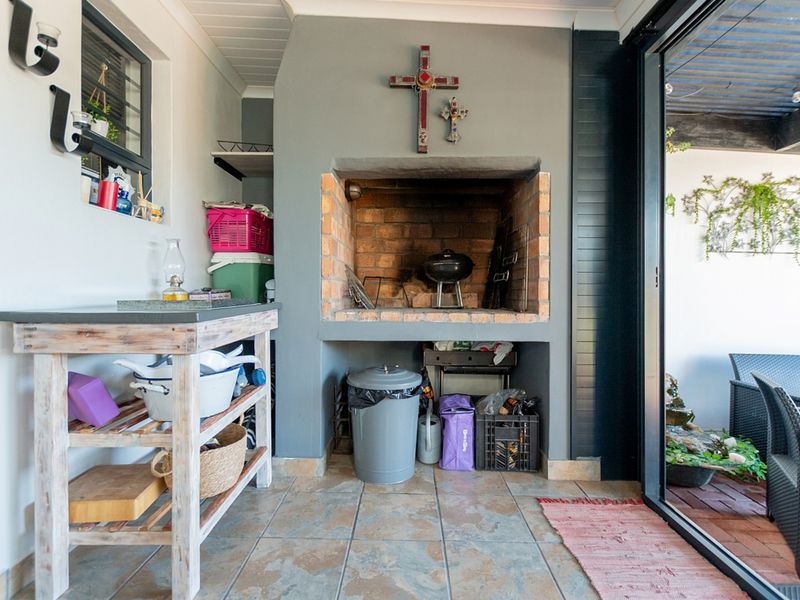 Covered patio area featuring a built-in brick braai, tiled flooring, and large sliding glass doors providing seamless access to the outdoor space.