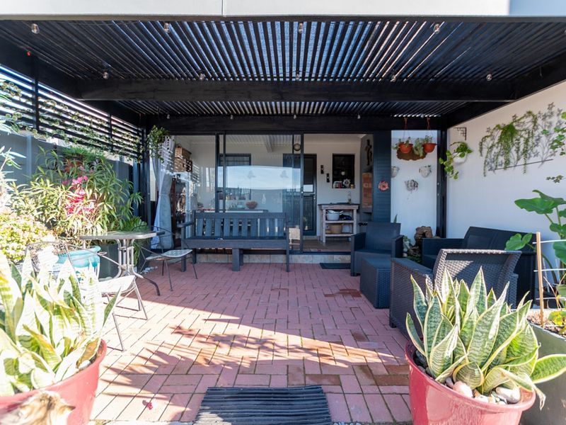 A covered outdoor patio area featuring a slatted pergola roof and brick paving, providing a seamless transition to the interior living space.