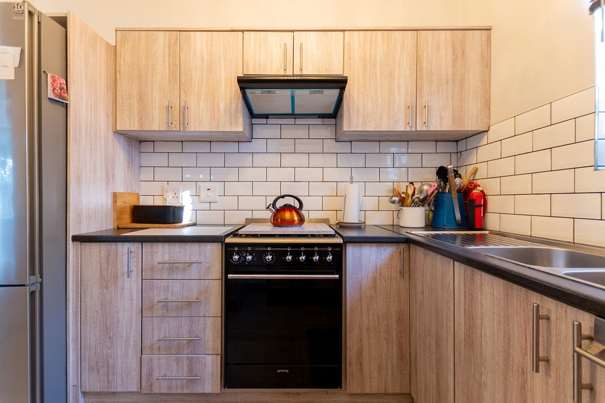 A well-maintained kitchen featuring wood-look cabinetry, a classic subway tile backsplash, black laminate countertops, and a built-in oven with an extractor fan.