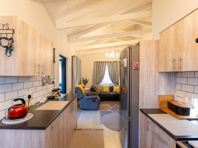 Open-plan kitchen and living area featuring light wood-finish cabinetry, subway tile backsplash, and a vaulted ceiling with exposed rafters.